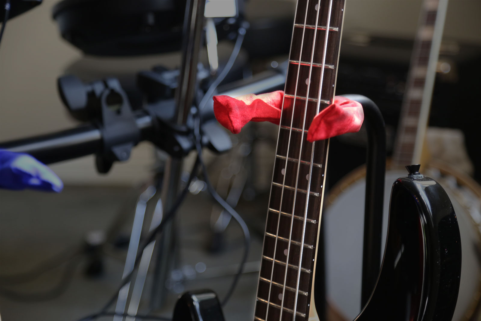 A bass guitar resting in a stand fitted with a red Axe Hugger cover.